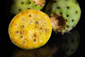 Close-up of fresh prickly pears lying against a dark background and reflected on the base. A cactus fruit is cut open. photo