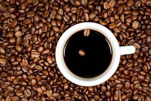 A cup of black coffee with two coffee beans floating in it stands against the background of many brown coffee beans photo