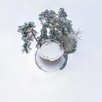 Winter tiny planet in snow covered pinery forest near lake with transformation of spherical panorama 360 degrees in abstract aerial view. Curvature of space photo
