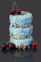 Three colorful donuts with blue icing and love pearls are stacked on top of each other. Above and to the side are red ripe cherries. The background is grey. photo