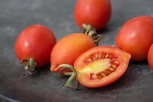 On an old, gray copper plate lies a group of small red tomatoes. The tomatoes are pointed at the front and come from Sicily. A tomato is cut open. photo