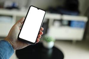 Mockup image of a man holding black mobile phone with blank white screen. In living room at home. photo