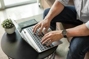 businessman sitting on sofa with mobile phone using laptop working at home to send and send reply to email Message customer service photo