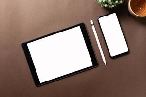 Black tablet with white blank screen is on top of brown paper with supplies. Top view, flat lay. photo