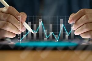 Businessman with a tablet on table And write on the screen That shows a business graph. The concept of starting a new business that goes better. Closeup of a man use pen with tablet. photo