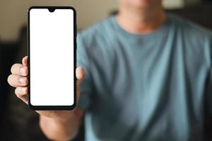 Smartphone blank screen presentation. A young man is holding a phone with a white empty screen mockup. a man is wear blue t-shirt in living room at home. photo