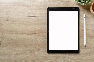 Black tablet with white blank screen is on top of wood desk table with supplies. Top view with copy space, flat lay. photo