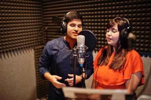 Young asian duet singers with microphone recording song in record music studio. photo