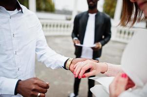 Wedding engagement ceremony with pastor. Multiethnic couple put ring each other. Relationships of african man and white european woman. photo