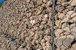 engineering structure made of stones behind metal wire netting to strengthen the river bank near the road bridge photo