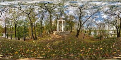 full seamless spherical hdri panorama 360 degrees view of autumn forest or park with bright sun shining through trees near concrete gazebo with columns in equirectangular projection, VR AR content photo