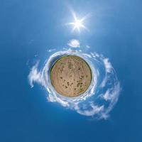 tiny planet in blue sky with sun and beautiful clouds. Transformation of spherical panorama 360 degrees. Spherical abstract aerial view. Curvature of space. photo