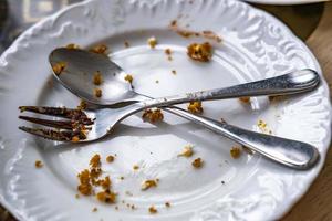 Empty dirty plate with spoon and fork on the table after breakfast photo