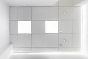 cassette suspended ceiling with square halogen spots lamps and drywall construction in empty room in apartment, clinic, office or house. Stretch ceiling white and complex shape. Looking up view photo