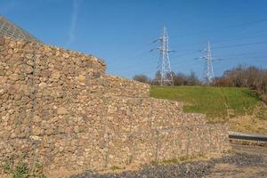 estructura de ingeniería hecha de piedras detrás de una malla metálica para fortalecer la orilla del río cerca del puente de la carretera foto