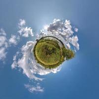 green tiny planet in blue sky with beautiful clouds. Transformation of spherical panorama 360 degrees. Spherical abstract aerial view. Curvature of space. photo