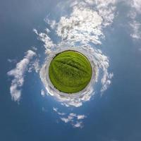 green tiny planet in blue sky with sun and beautiful clouds. Transformation of spherical panorama 360 degrees. Spherical abstract aerial view. Curvature of space. photo