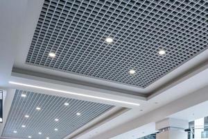 suspended and grid ceiling with halogen spots lamps and drywall construction in empty room in store or house. Stretch ceiling white and complex shape. photo