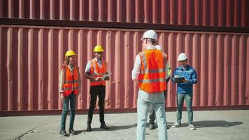 un grupo de trabajadores multirraciales con uniformes de seguridad parados en fila y discutiendo con el gerente caucásico en el muelle de logística con pilas de contenedores, envío de mercancías e industria de transporte de carga. video