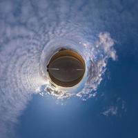 tiny planet in blue sky with beautiful clouds. Transformation of spherical panorama 360 degrees. Spherical abstract aerial view. Curvature of space. photo