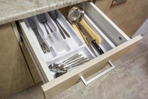 set of knives, forks and  spoons on the shelf in the kitchen cabinet photo