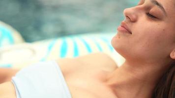 Cerca de una hermosa mujer joven en bikini blanco y negro salones en un flotador de flamencos en una piscina video