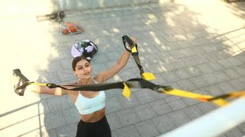 Fit young woman exercises in public space using suspension bands video