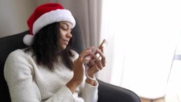 jong vrouw in de kerstman hoed toepassingen slim telefoon zittend door een venster