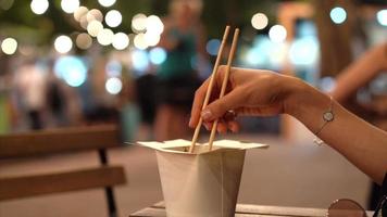stänga upp av feminin hand använder sig av ätpinnar i en kinesisk ta ut låda på ett utomhus- tabell video