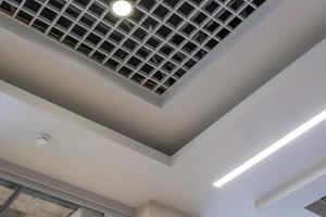 suspended and grid ceiling with halogen spots lamps and drywall construction in empty room in store or house. Stretch ceiling white and complex shape. photo
