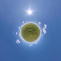 green tiny planet in blue sky with sun and beautiful clouds. Transformation of spherical panorama 360 degrees. Spherical abstract aerial view. Curvature of space. photo