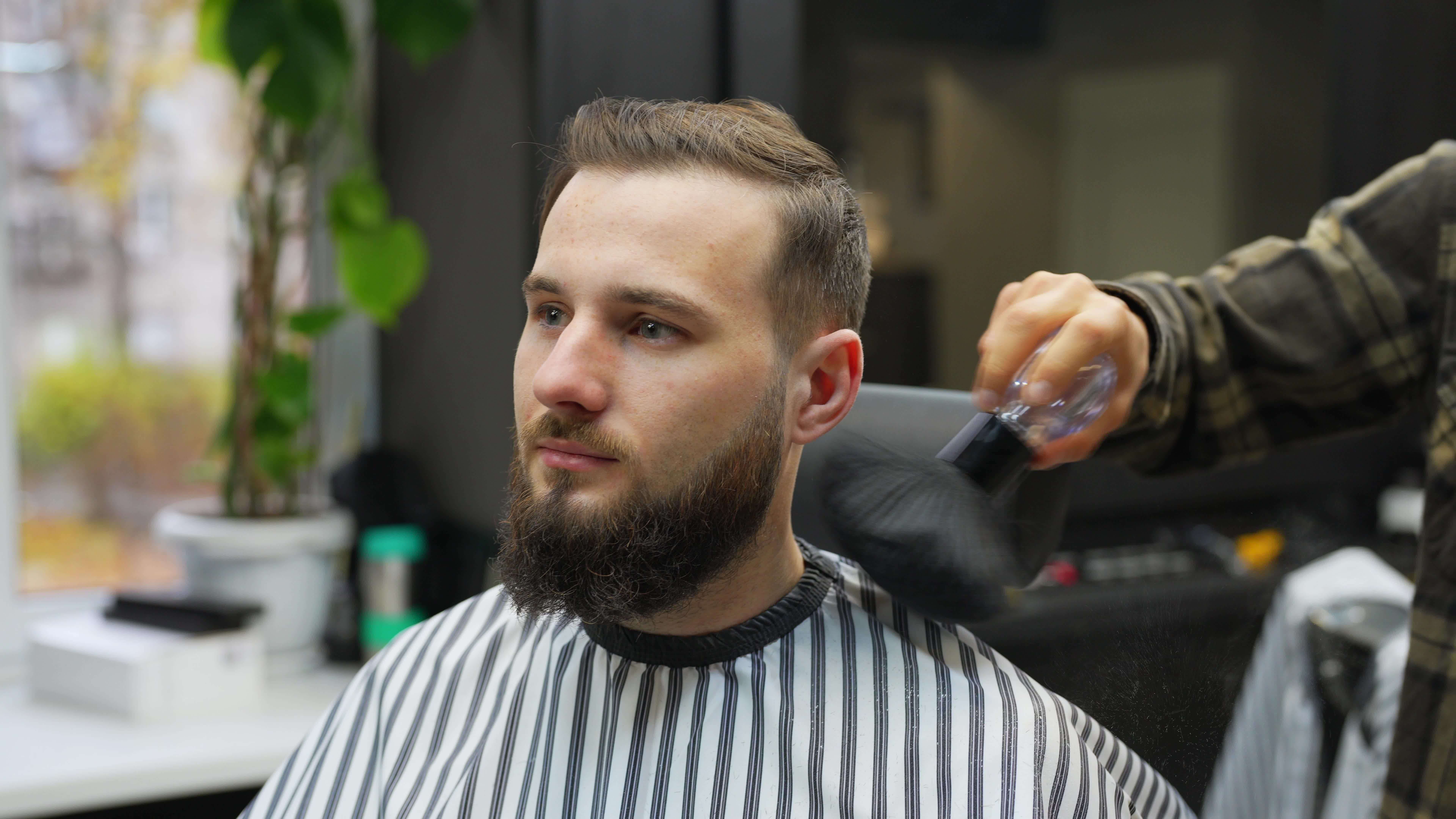 Barber brushes hair off ears and neck of male client seated in chair
