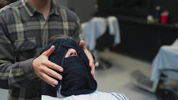Barber places warm towel over man's face as he relaxes in the chair video