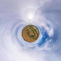 green tiny planet in blue sky with beautiful clouds. Transformation of spherical panorama 360 degrees. Spherical abstract aerial view. Curvature of space. photo