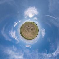 green tiny planet in blue sky with beautiful clouds. Transformation of spherical panorama 360 degrees. Spherical abstract aerial view. Curvature of space. photo