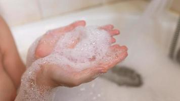 Young woman soaking in bubble bath laughs and blows suds from hands video