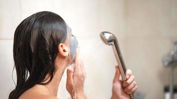 Young woman rinses clay mask off face in the shower video