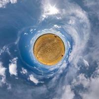 green tiny planet in blue sky with sun and beautiful clouds. Transformation of spherical panorama 360 degrees. Spherical abstract aerial view. Curvature of space. photo