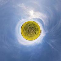 yellow little planet transformation of spherical panorama 360 degrees. Spherical abstract aerial view in rapeseed field with awesome beautiful clouds. Curvature of space. photo