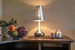 burning candles and a vase with fruit apples and grapes on the table near the lamp photo