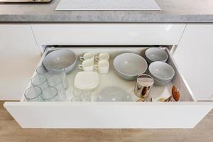 set of plates, cups, knives, forks and wine glasses on the shelf in the kitchen cabinet photo