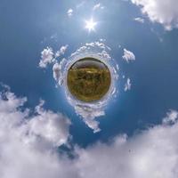 green tiny planet in blue sky with beautiful clouds. Transformation of spherical panorama 360 degrees. Spherical abstract aerial view. Curvature of space. photo