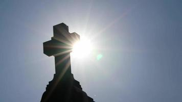 cruz sagrada brillante con rayos de sol brillantes a través del follaje y el cielo brilla una luz de fe espiritual y cristianismo con símbolo de muerte religiosa y resurrección de dioses en la tumba del cementerio al atardecer video