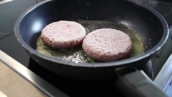 hamburguesas congeladas carne de hamburguesa chisporroteando en una sartén caliente con grasa y aceite como deliciosas albóndigas de barbacoa caseras como un almuerzo de comida rápida poco saludable con muchas calorías y colesterol en una sartén video