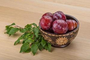 ciruelas frescas en un recipiente sobre fondo de madera foto