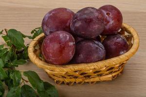 Fresh plums in a basket on wooden background photo