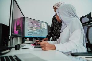 Friends at the office two young Afro American modern Muslim businesswomen wearing scarf in creative bright office workplace with a big screen photo