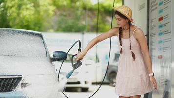 Young woman in pink dress and straw hat washes a car