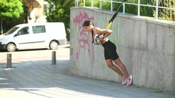 Fit young woman exercises in public space using suspension bands video