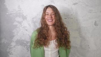 Young woman with long red curly hair laughs looking toward camera video